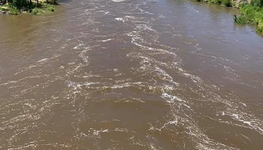 The image shows a muddy, fast-flowing river with sediment and foam on its surface.