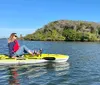 A person is casually seated on a yellow kayak enjoying the calm waters near a green-covered coastline under a clear blue sky