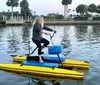A person is standing on a water bike a yellow aquatic contraption with pedals floating on calm waters near a dock during dusk