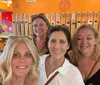 Four smiling women take a selfie together in a colorful candy store with dispensers filled with various sweets in the background