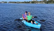 Two people are smiling and enjoying a sunny day out on the water in a blue tandem kayak.