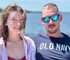 A man and a woman are smiling for a photo with a body of water in the background on a sunny day