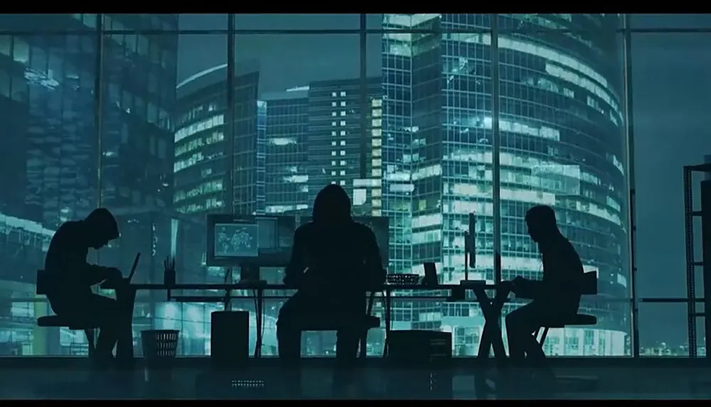 Three silhouetted figures are working at desks with screens in a dimly lit office overlooking a cityscape at night