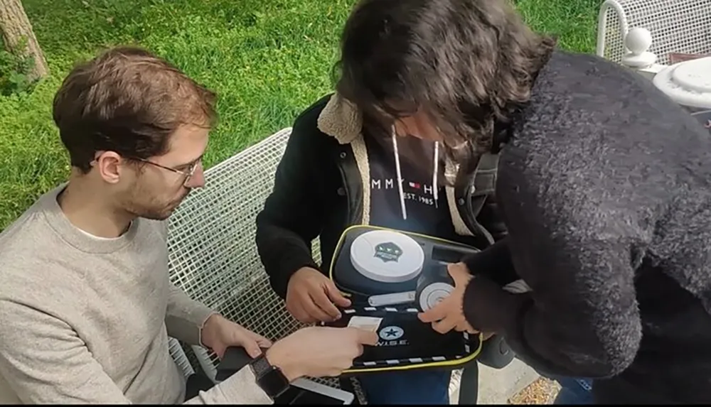 Two people are attentively examining an electronic device outdoors