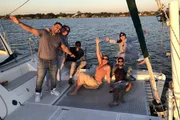 A group of people are joyfully posing on a boat during what appears to be a sunset sailing trip.