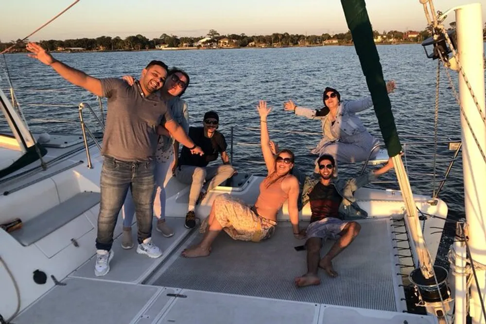 A group of people are joyfully posing on a boat during what appears to be a sunset sailing trip