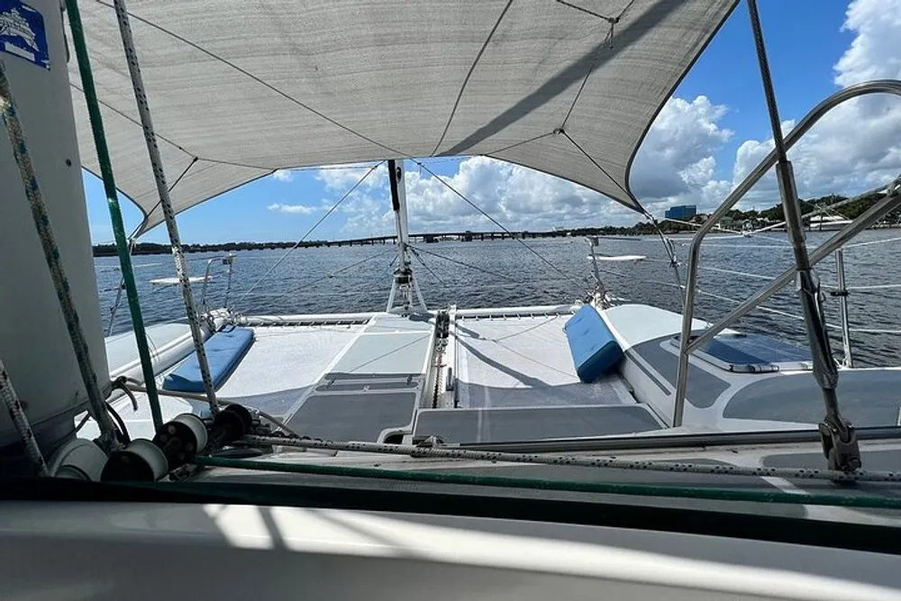 The image shows a view from the back of a sailboat looking forward as it sails on the water under a blue sky with scattered clouds