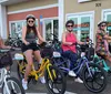 Four people are smiling and posing with colorful electric bikes in front of a bike rental shop