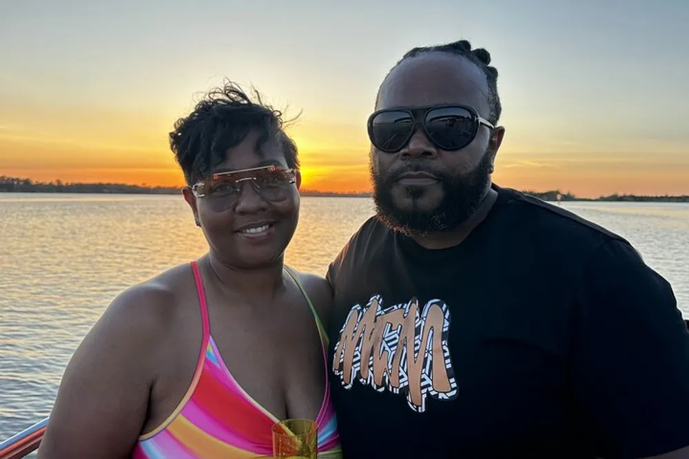 Two people are posing for a photo with a beautiful sunset over the water in the background