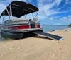 A pontoon boat is docked on a sandy shore under a blue sky with scattered clouds