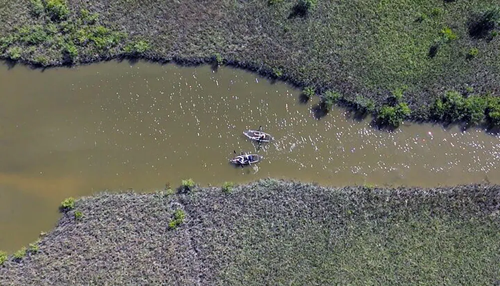 Two boats with people are floating on a winding river surrounded by greenery viewed from above