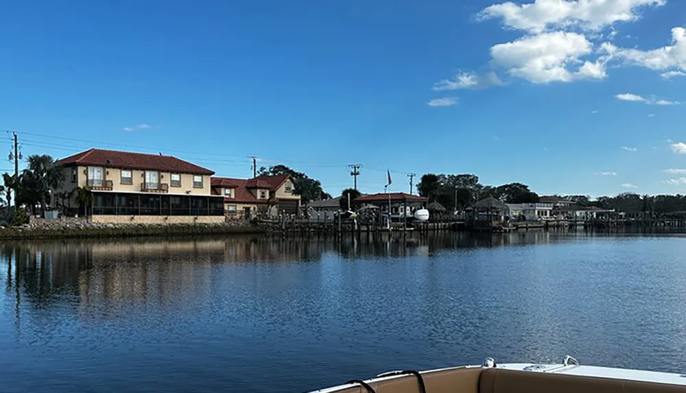 The image captures a tranquil waterway with residential buildings along its bank reflecting a serene lifestyle under a blue sky scattered with clouds