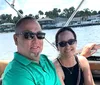 Two people are smiling for a selfie on a boat with waterfront properties in the background