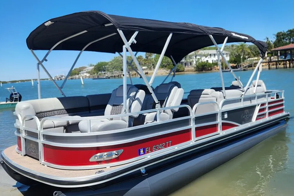 A pontoon boat with a canopy is docked in calm blue waters on a sunny day