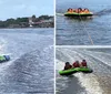 Three people are wearing life jackets excitedly riding a towable water tube behind a boat with coastal buildings in the background