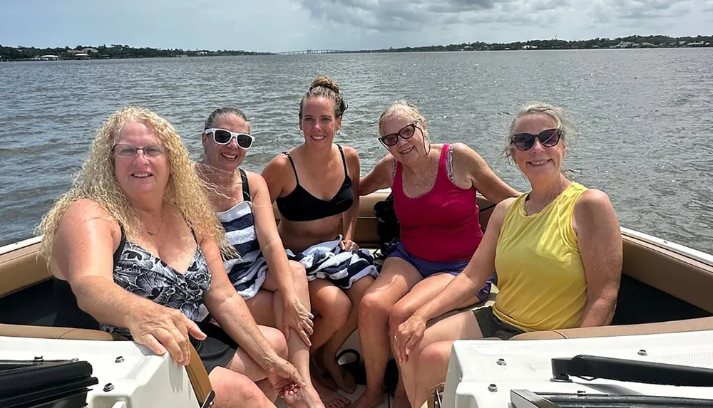 Five individuals are smiling while seated on a boat enjoying a sunny day on the water