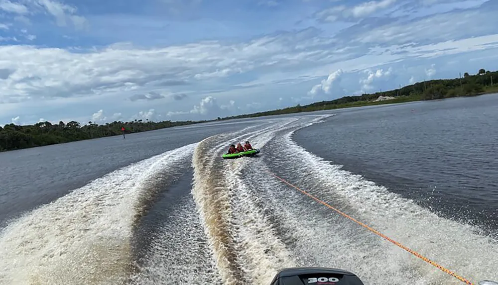 A speedboat is pulling a colorful inflatable raft with several passengers on a winding water path on a sunny day