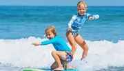 Two children are happily surfing together on a bright, sunny day at the beach.