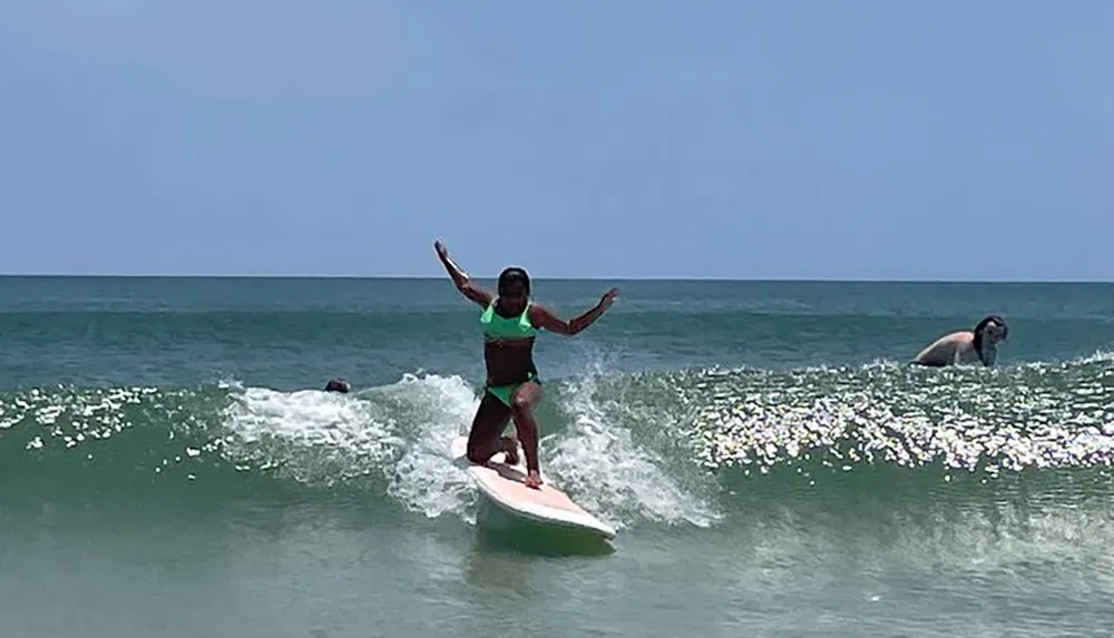 A person is balancing on a surfboard riding a small wave in the ocean with others in the water nearby