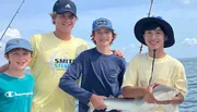 Four smiling youths pose on a boat with one holding a small shark they appear to have caught while fishing.