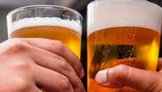 Two hands holding pints of beer in a social toast or cheers gesture.