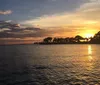 The image captures a sailboat gliding on calm waters with the sun setting in the background casting a golden reflection on the waters surface