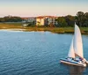 The image captures a sailboat gliding on calm waters with the sun setting in the background casting a golden reflection on the waters surface