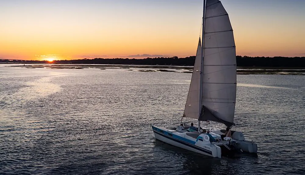 A sailboat cruises on tranquil waters against the backdrop of a beautiful sunset