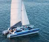 A sailboat glides across calm waters near a coastal settlement during a tranquil sunset