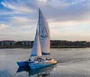 A sailboat glides across calm waters near a coastal settlement during a tranquil sunset