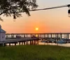 This collage features four different coastal scenes including a boat at a pier a solitary tree against a twilight sky waterfront homes on stilts and a sunset view from a dock with a destroyed structure in the water