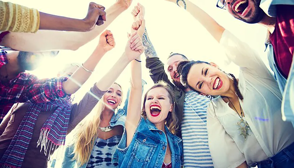 A group of joyful people are raising their arms together in a display of happiness and camaraderie under a sunny sky