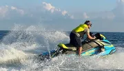 A person in a life vest is riding a jet ski on the sea, creating a splash of water around them.