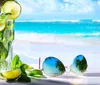 A refreshing glass of mojito alongside a pair of sunglasses is laid out on a table with a tropical beach backdrop