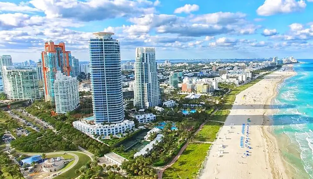 The image shows a scenic aerial view of a coastal city with modern high-rise buildings alongside a long sandy beach and clear blue waters