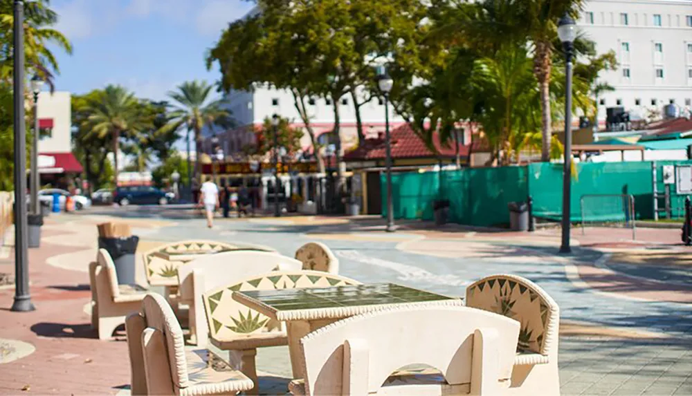 Sunlight bathes a pedestrian street lined with palm trees and equipped with sculptural benches creating a relaxed urban scene