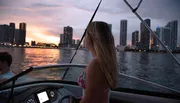 A woman is admiring a sunset from a boat with a city skyline in the background.