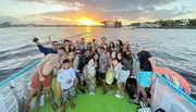 A joyful group of people are taking a selfie on a boat during a sunset.