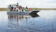 A group of tourists is enjoying a ride on an airboat through a waterway with sparse vegetation.
