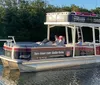 A pontoon boat with passengers is cruising near a lush shoreline under bright sunlight