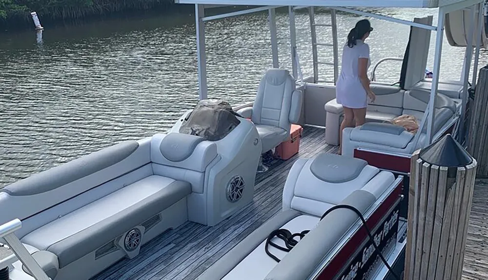 A person is standing on a pontoon boat docked at a wooden pier by the water