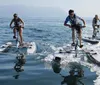 Three individuals are riding on hydrofoil bikes across a calm sea surface