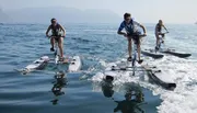 Three individuals are riding on hydrofoil bikes across a calm sea surface.