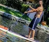 Four people are standing on paddleboards in a waterfront canal with a luxury yacht and upscale residence in the background