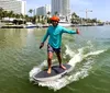 A person is balancing on a motorized surfboard gliding across the water with urban buildings in the background