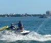 A person is riding a jet ski across a body of water with a city skyline in the background