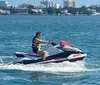 A person is riding a jet ski on a sunny day with a coastal city skyline in the background