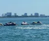 A person is riding a jet ski on a sunny day with a coastal city skyline in the background