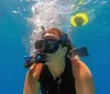 A person is snorkeling underwater exhaling bubbles near a floating yellow snorkel tube
