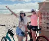 Two people are posing with raised arms next to their bicycles on Hollywood Beach near a sign listing beach regulations